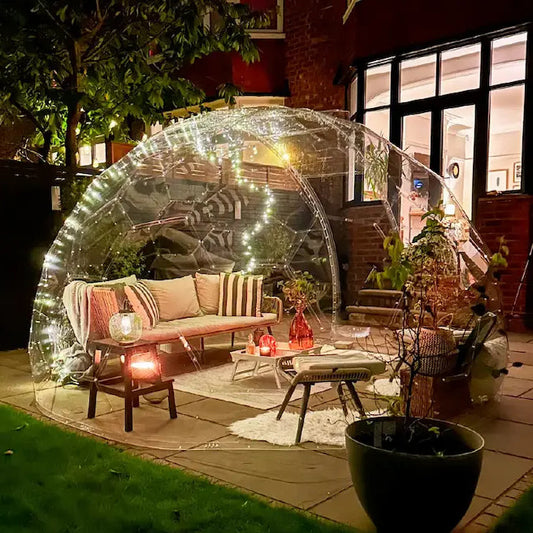 A GeoDomeX dome glowing with warm lights in a garden at dusk